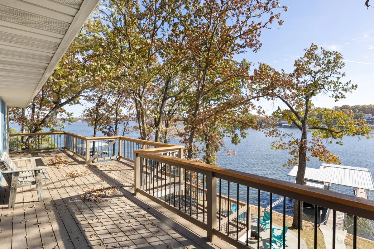 A tranquil deck scene overlooking the lake with autumn foliage in the background. The deck is bordered by a railing, providing an elevated spot to relax and enjoy nature, with plenty of space for pets to roam safely.