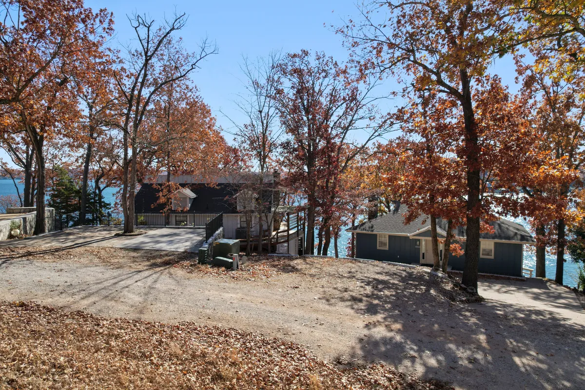 A tranquil waterfront view with rich autumn foliage in the foreground and two houses nestled along the shoreline. The calm water reflects the trees, offering a peaceful and inviting atmosphere. The setting suggests easy access to nature trails, water activities, and seasonal outdoor fun.