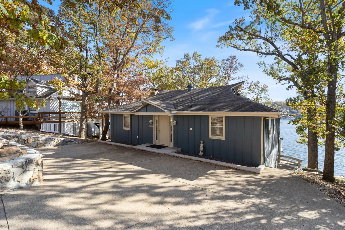 This image captures the front entrance of the house, with a landscaped yard and a glimpse of the lake beyond. The inviting porch and natural surroundings set a tranquil, welcoming tone, highlighting both private access and the property's connection to the lake.