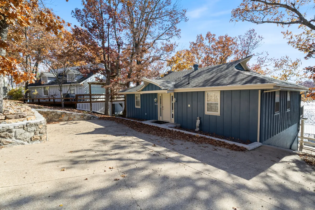 This exterior shot displays the striking blue exterior of the house among mature trees, with the driveway leading up to the home. The peaceful setting highlights the feeling of escape and serves as a visual anchor for the property's sense of place.