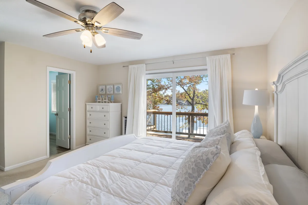 A calm and inviting bedroom scene with a comfortable bed, a window framing lush greenery outside, and a dresser and lamp for personal comfort. The color palette is soft and neutral, designed to promote restful sleep and quiet moments of reflection.