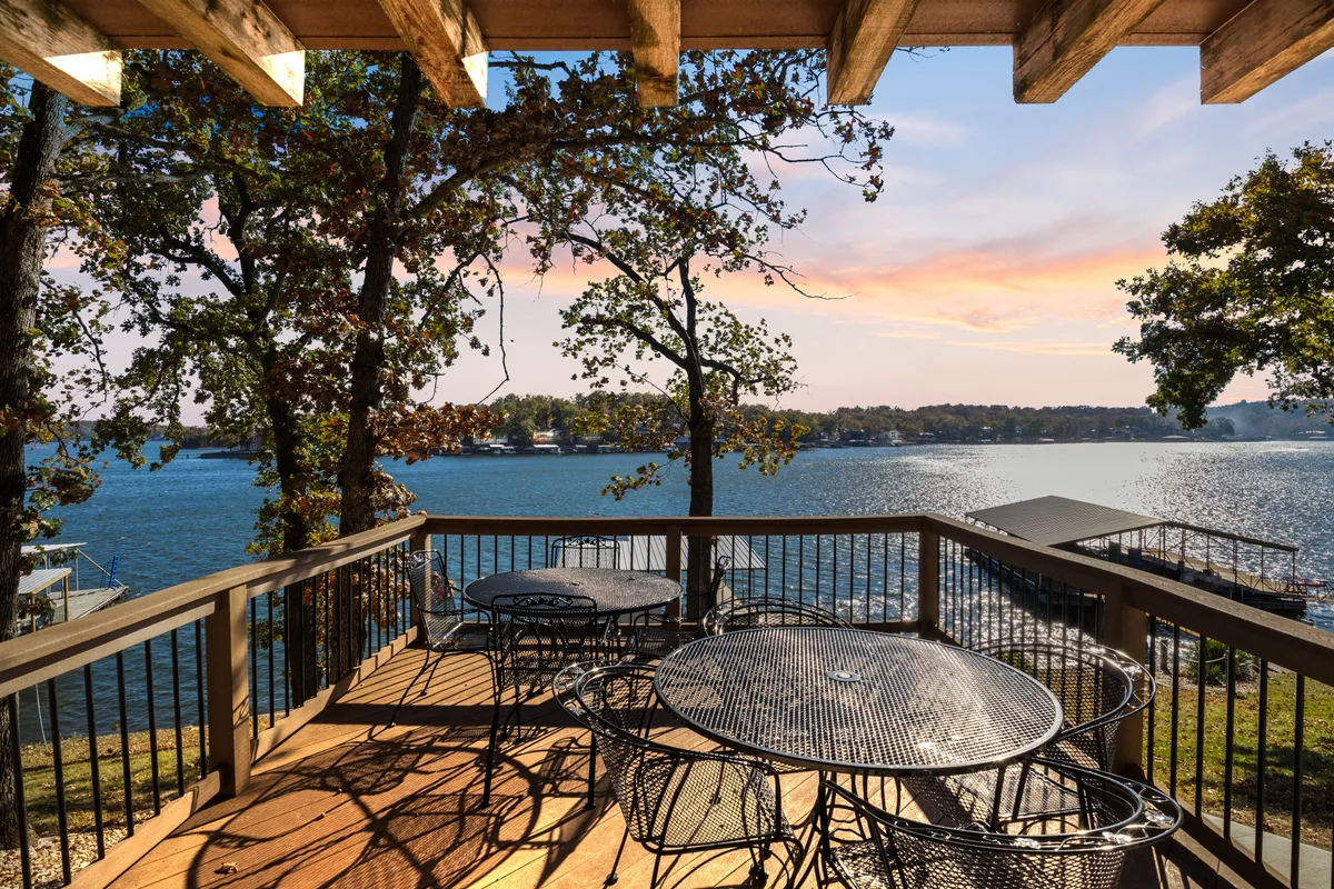 An outdoor scene with comfortable seating overlooking the waterfront, framed by trees and featuring a peaceful sunset. The setup encourages relaxation, socializing, and enjoying the shared community amenities such as pools or trails.