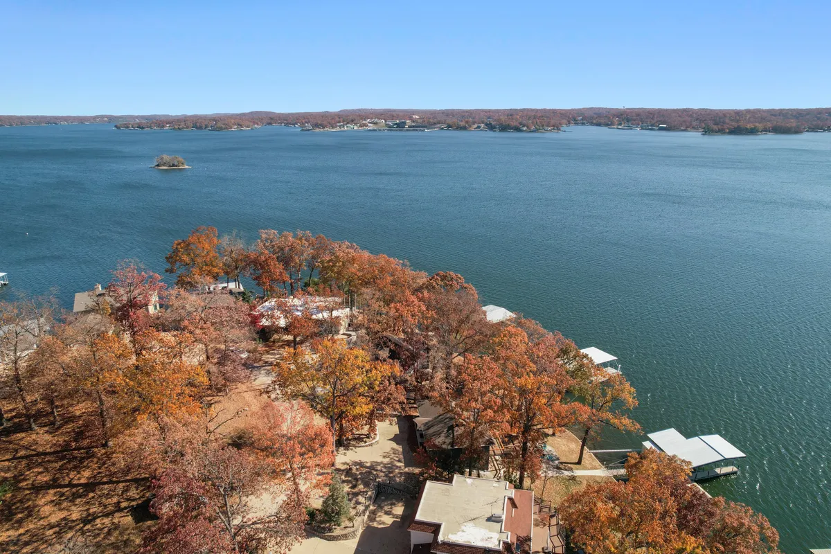 A wide shot of the lake framed by vibrant autumn foliage, featuring a dock that stretches out into the water and neighboring houses along the shoreline. The scene encapsulates a range of lakeside activities, with clear visual cues for boating, fishing, and casual gatherings.
